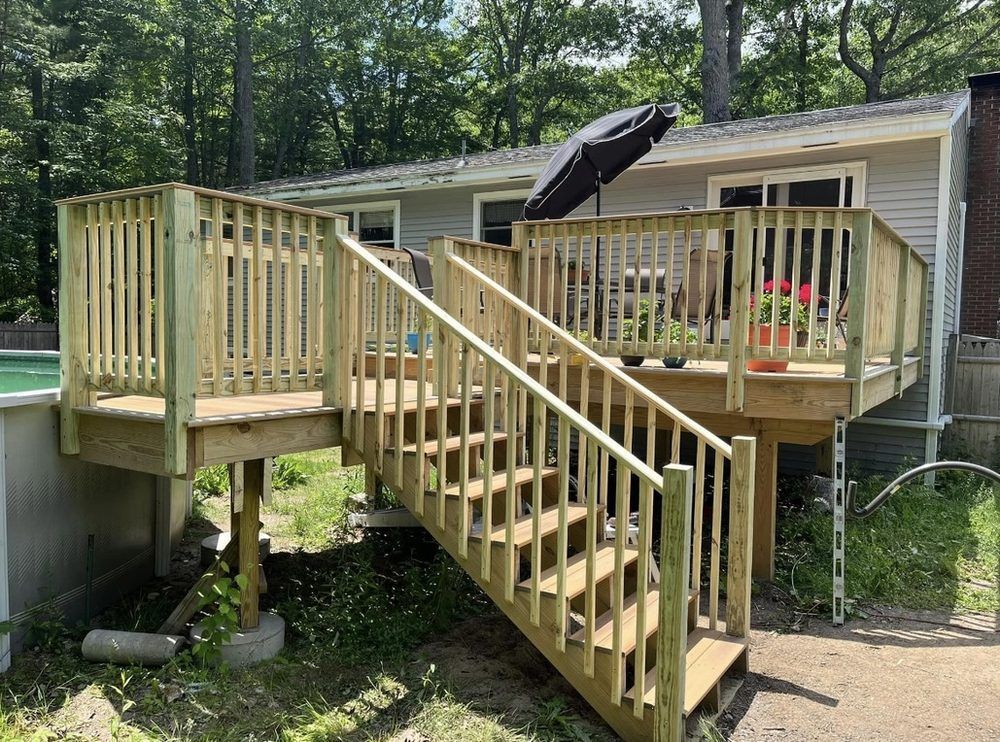 Wooden deck with stairs leading to a house, with an umbrella and plants, next to a pool.