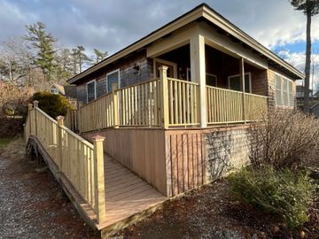A wooden deck outside a house, with white chairs, a small shed, and grassy yard.