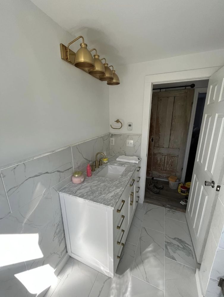 Bathroom with marble-look tile, white vanity, gold fixtures, and an open doorway leading to a rustic door.