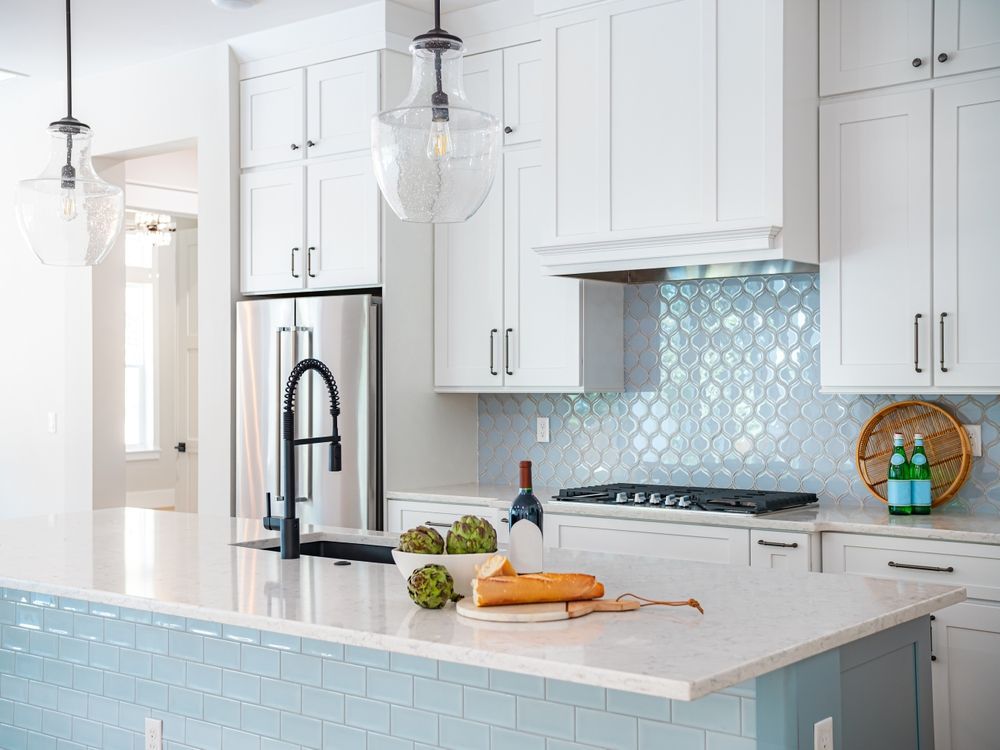 A kitchen with white cabinets , blue tiles , stainless steel appliances and a large island.