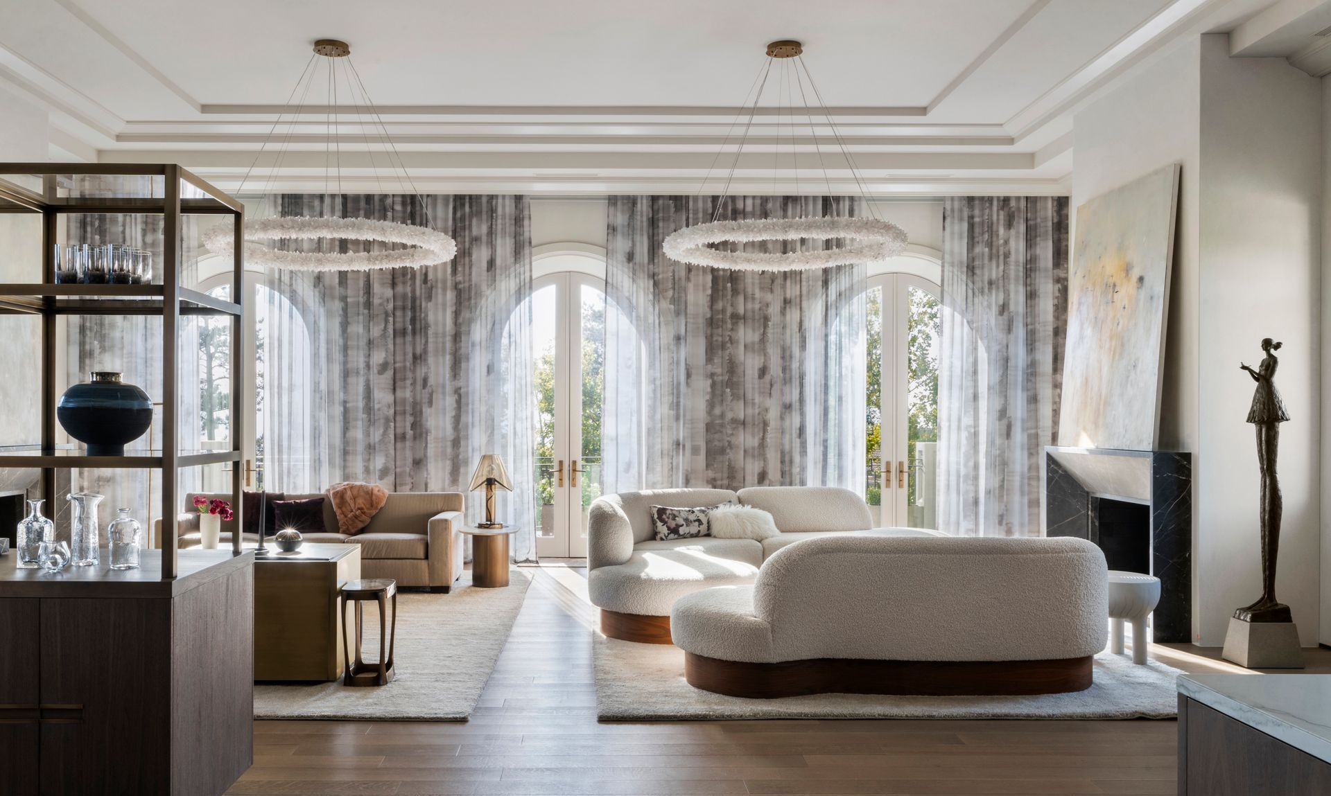 Elegant living room with sheer drapery covering tall arched windows, soft seating, and modern chandeliers