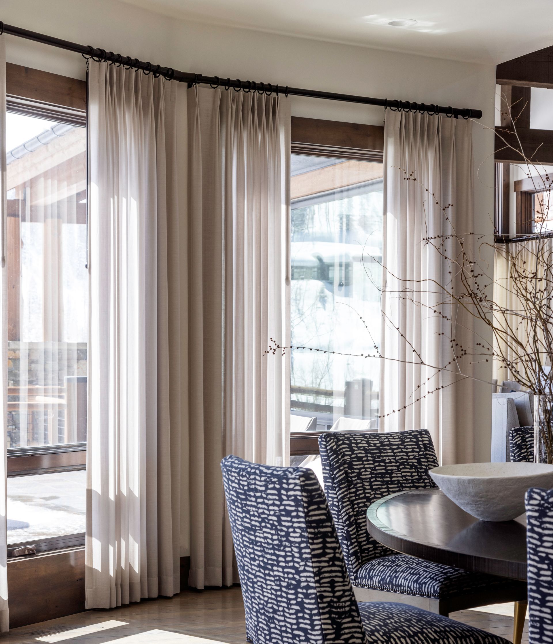 Soft sheer drapery panels frame large windows, filtering natural light in a bright and elegant living space
