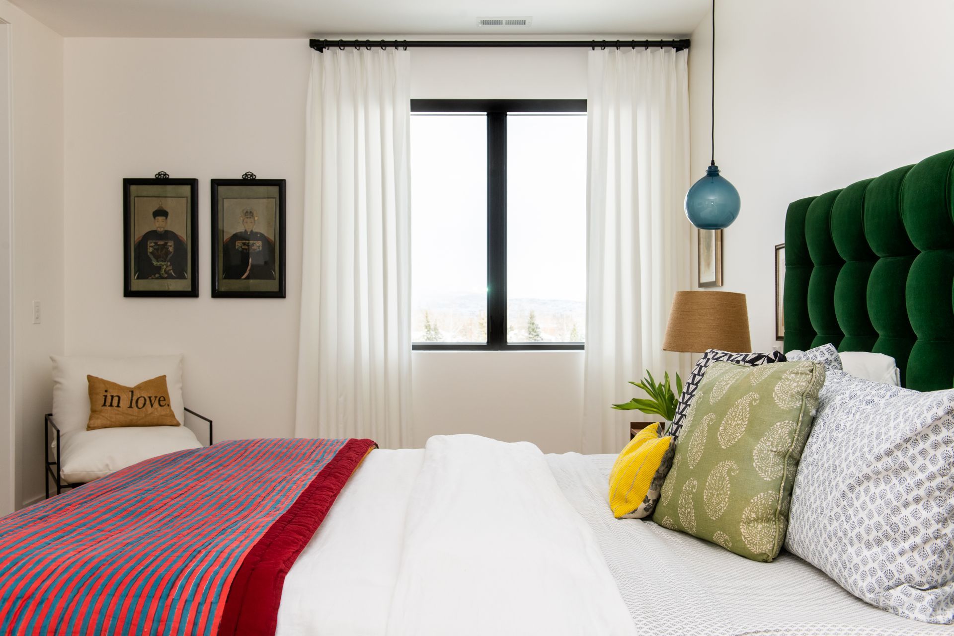 Bedroom with white curtain panels over a large window, green upholstered headboard, and modern decor