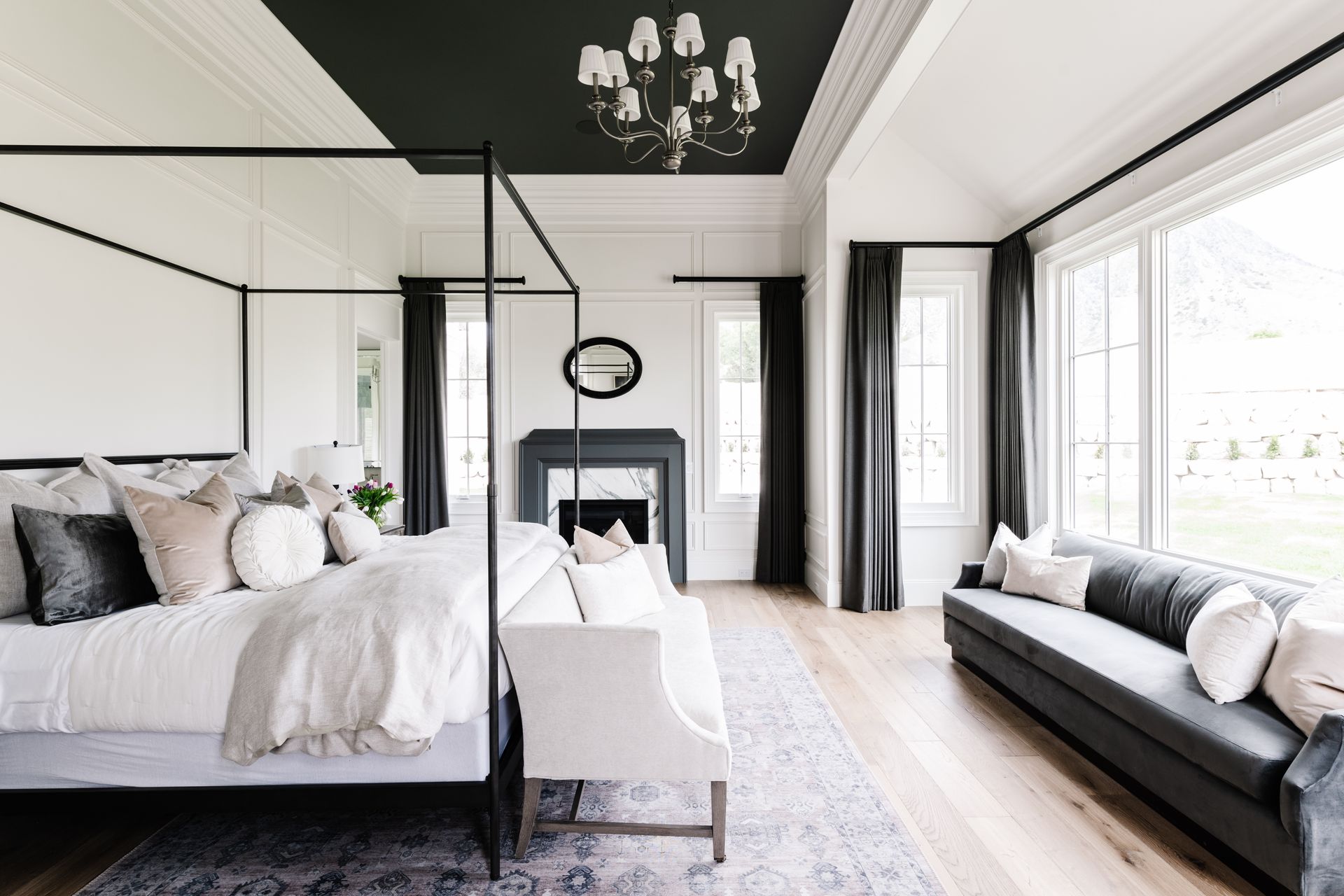 Luxury bedroom with floor-to-ceiling windows, black drapery panels, canopy bed, and fireplace seating area