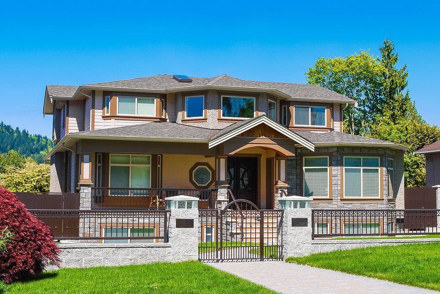 Two-story Craftsman-style house with brown siding, fence, and green lawn under a blue sky.
