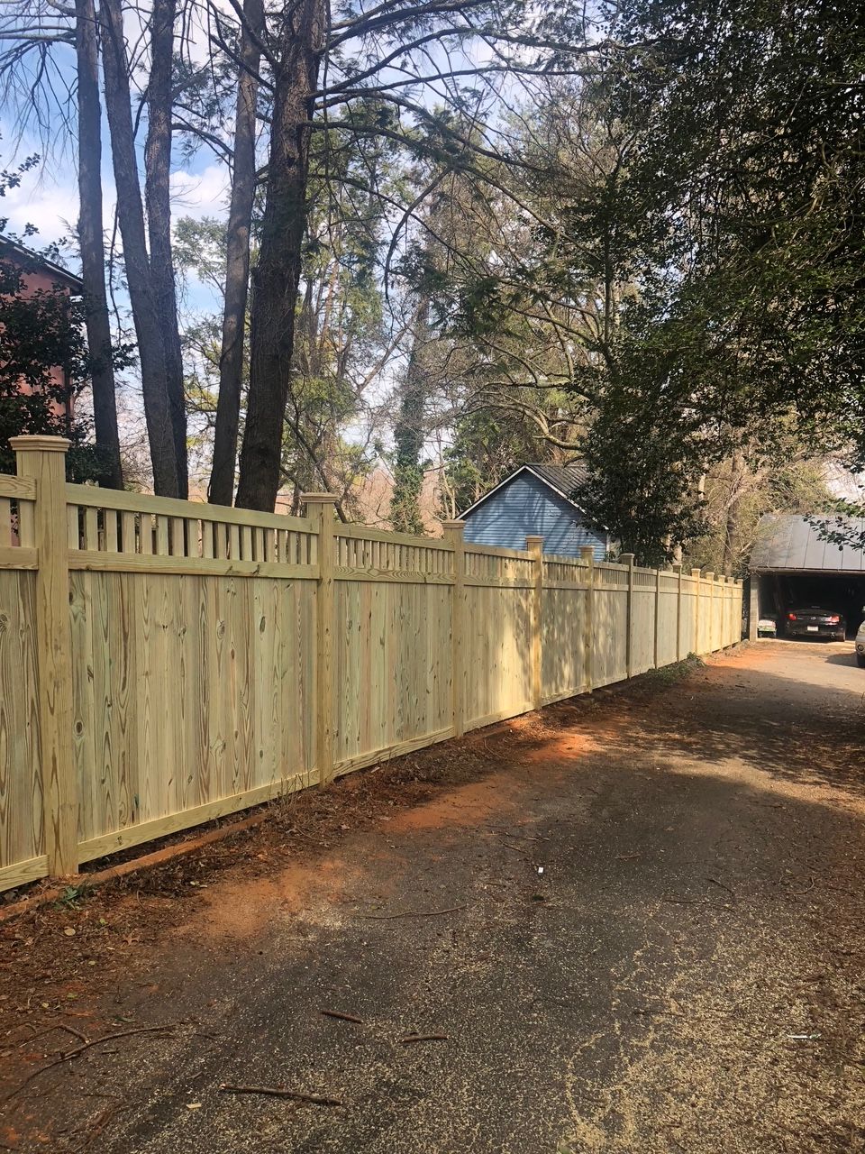 Wooden fence along a driveway, with trees in the background.