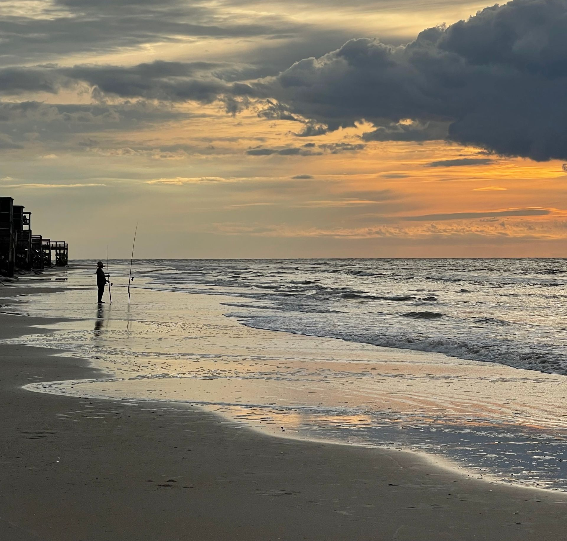 Sunset over a quiet beach with gentle waves and a cloudy sky reflecting on wet sand