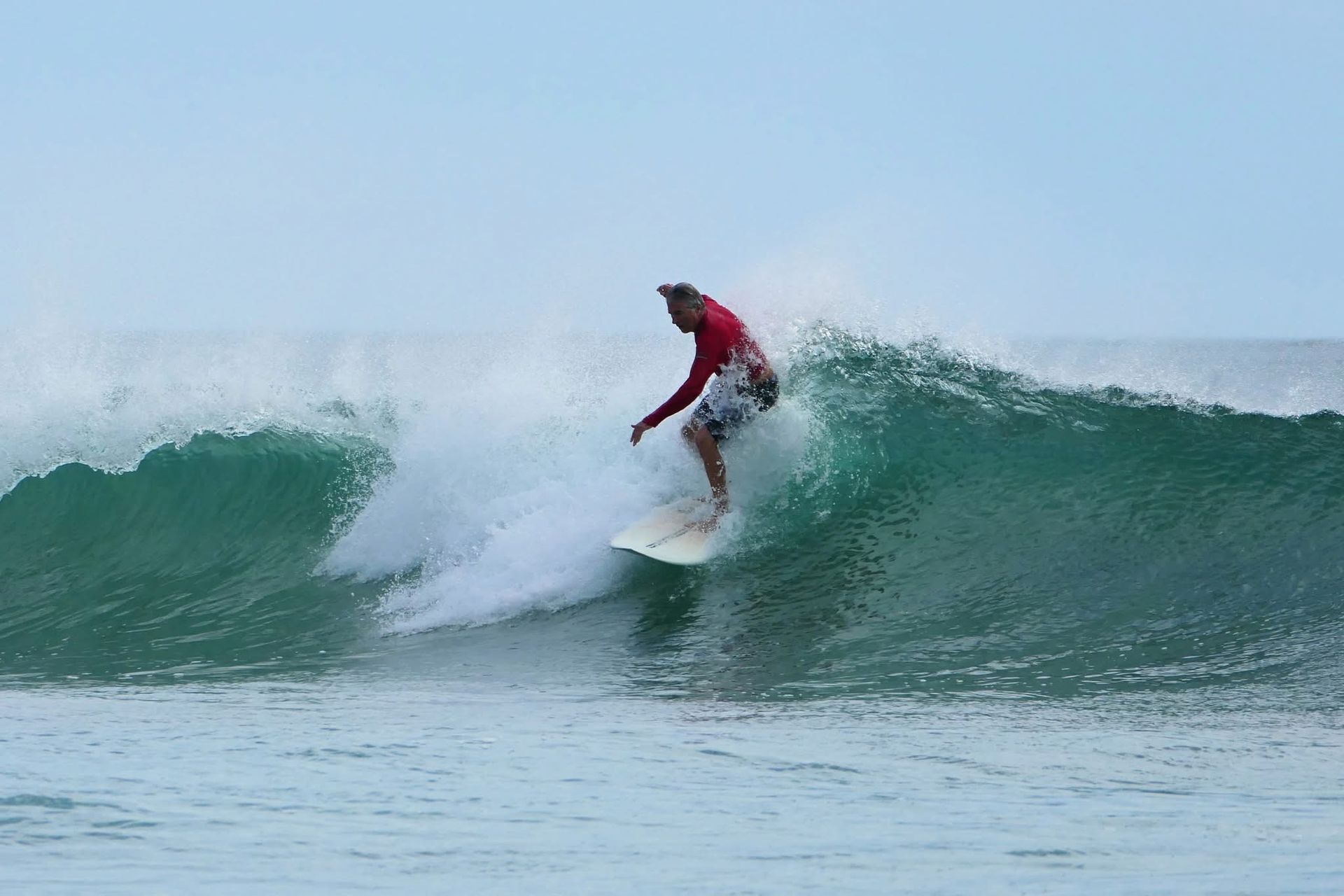 Surfer in a red wetsuit riding a green wave under a cloudy sky