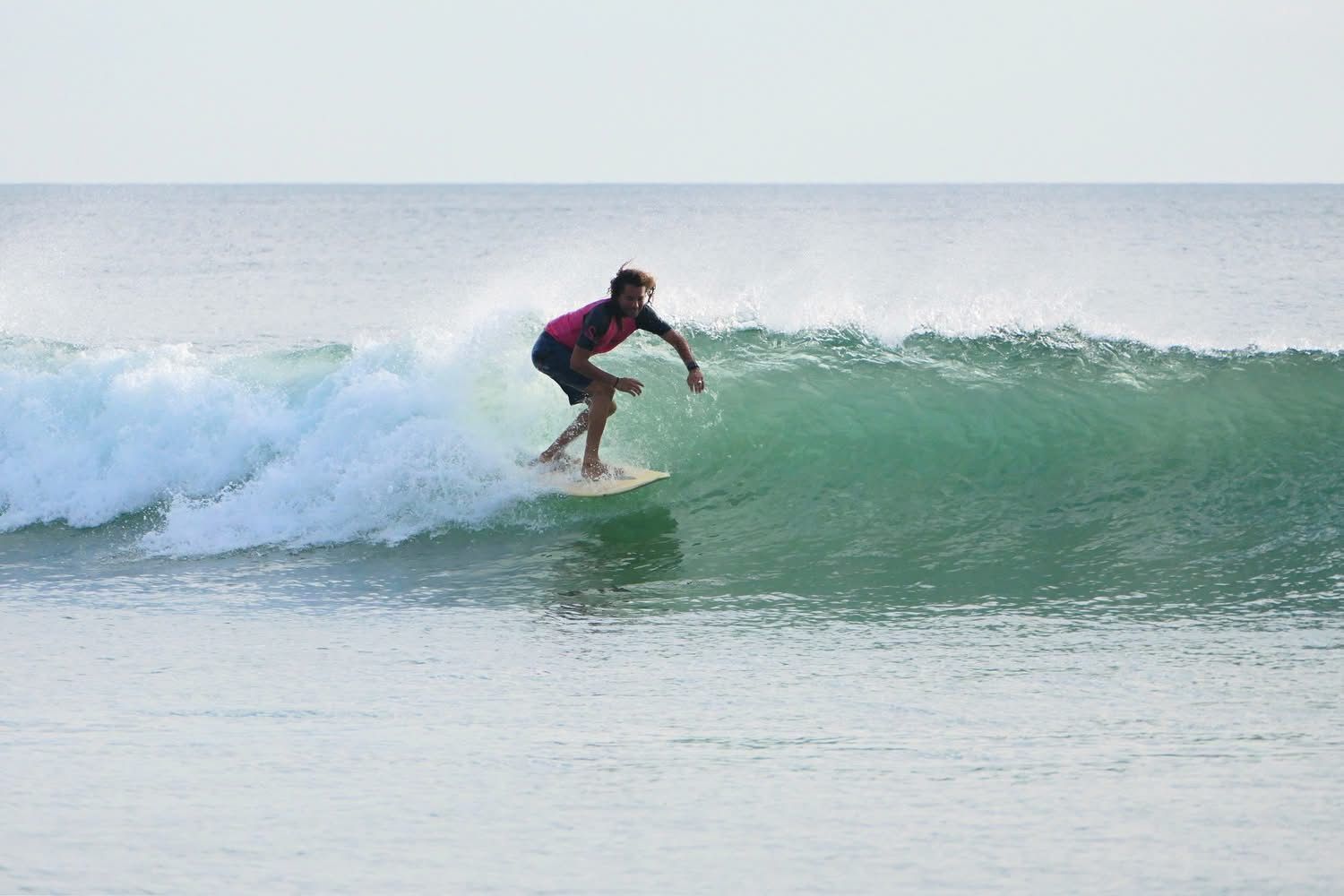 Surfer riding a small green wave in calm ocean water
