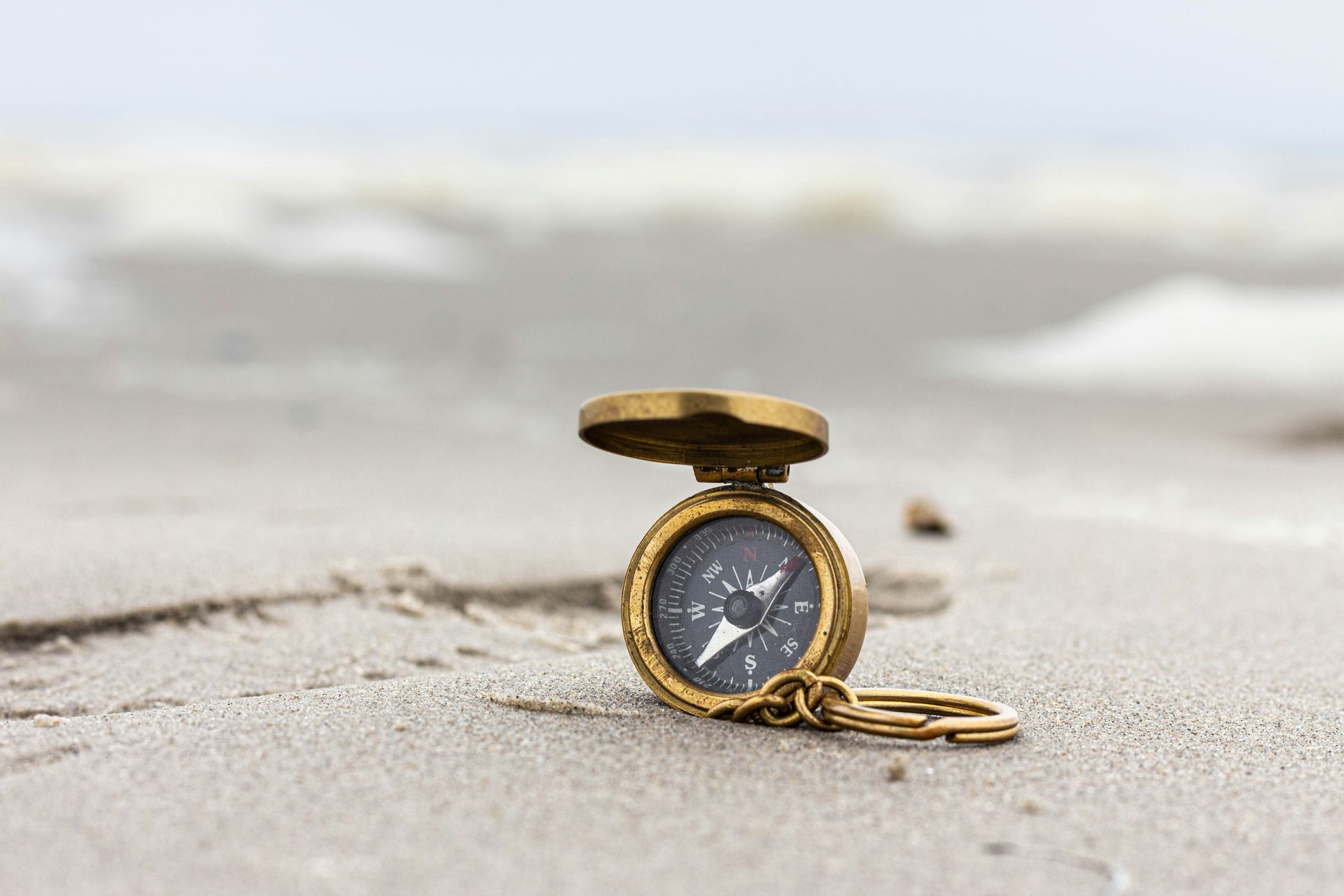 Gold pocket watch lying open on a sandy beach with blurred waves in the background