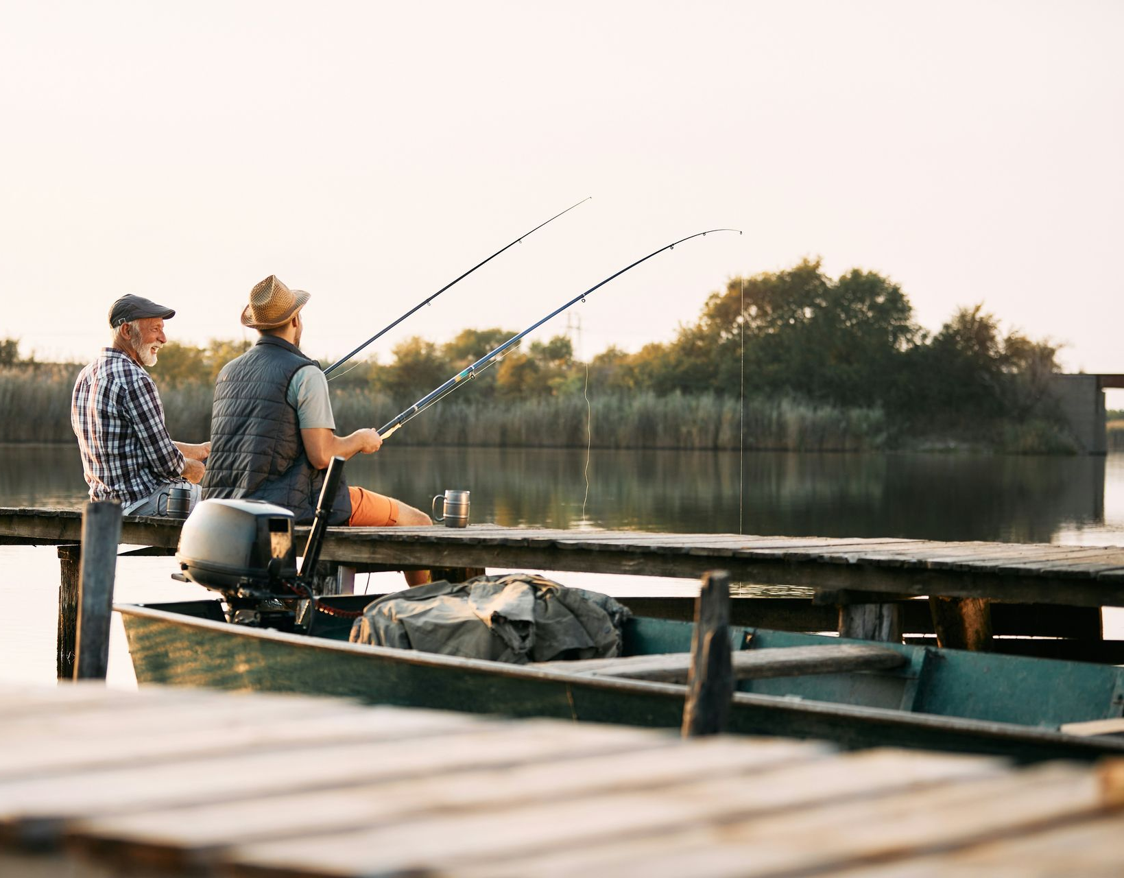 Two anglers on a dock fishing at sunset beside a calm lake