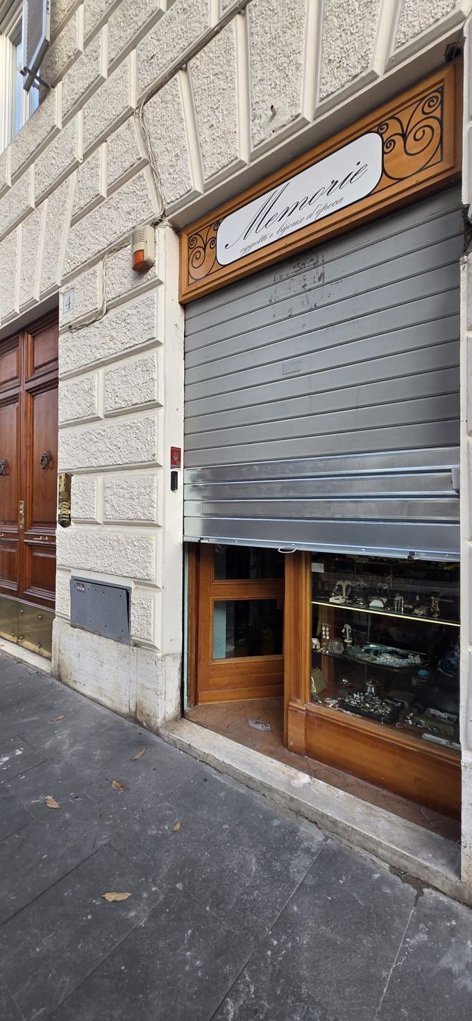 Negozio chiuso con serranda in metallo grigio, finiture in legno e una piccola vetrina su un edificio in pietra.