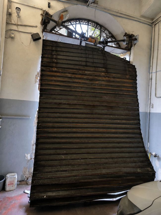 clicca sulla foto Una saracinesca metallica chiusa blocca l'ingresso di un edificio sotto un'apertura ad arco.