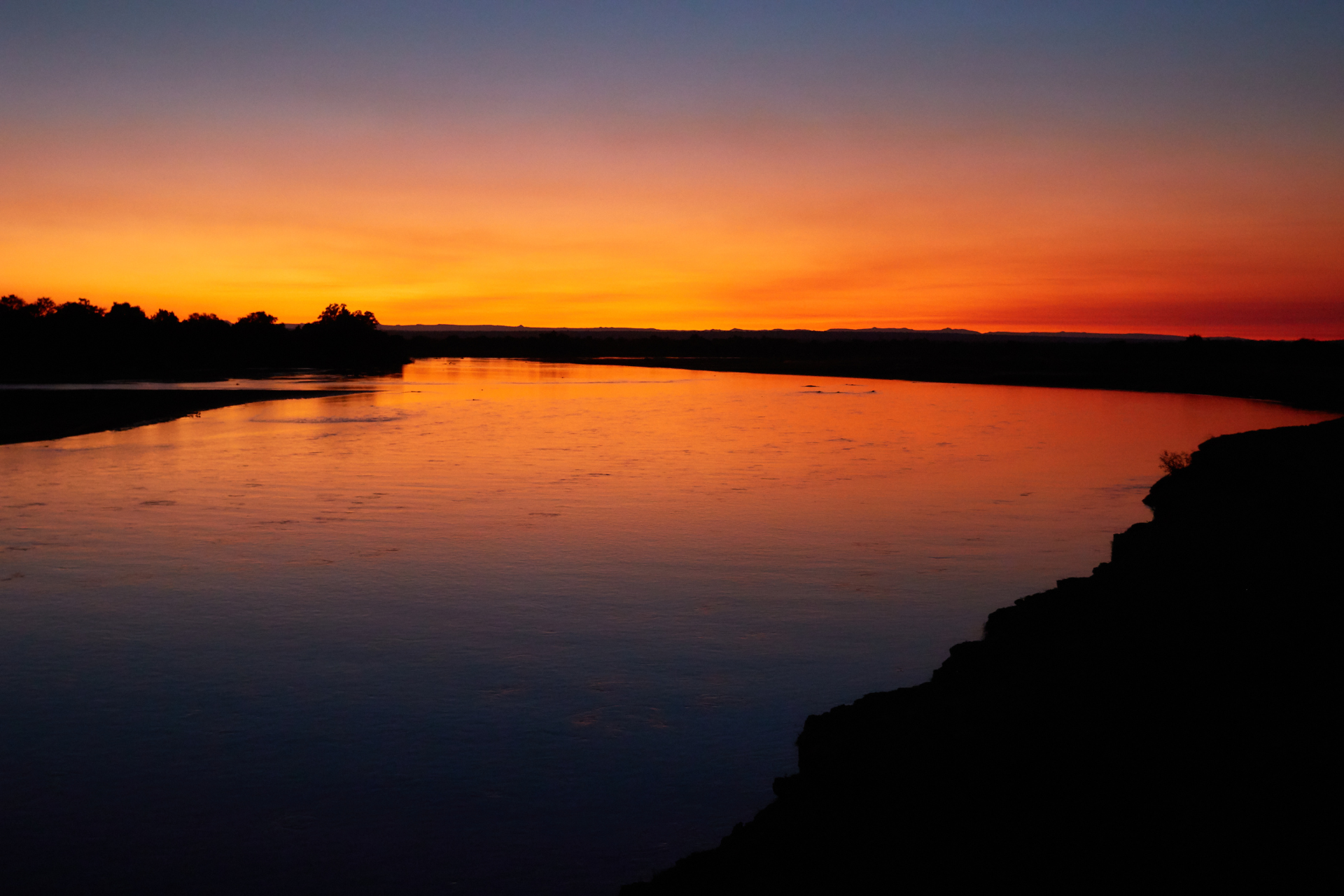A river with a sunset in the background and trees in the foreground.
