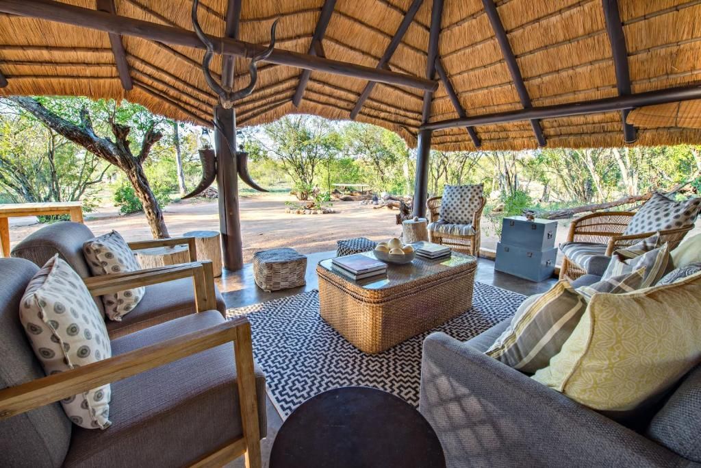 Outdoor seating area with thatched roof, surrounded by trees.