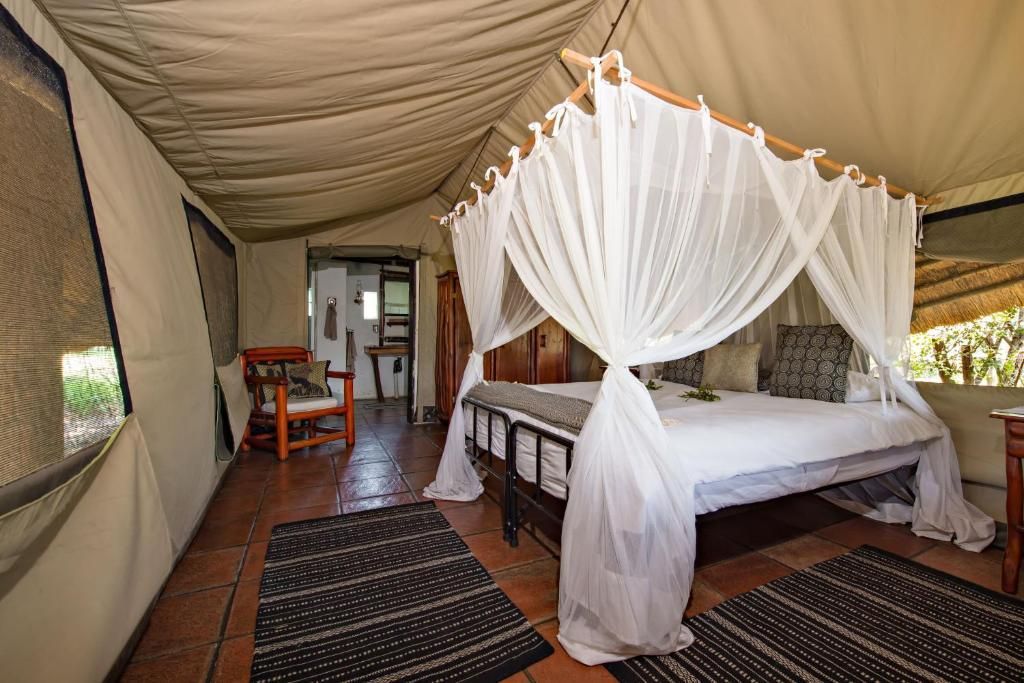 Inside of a luxury safari tent bedroom with a canopy bed, rugs, and open doorway.