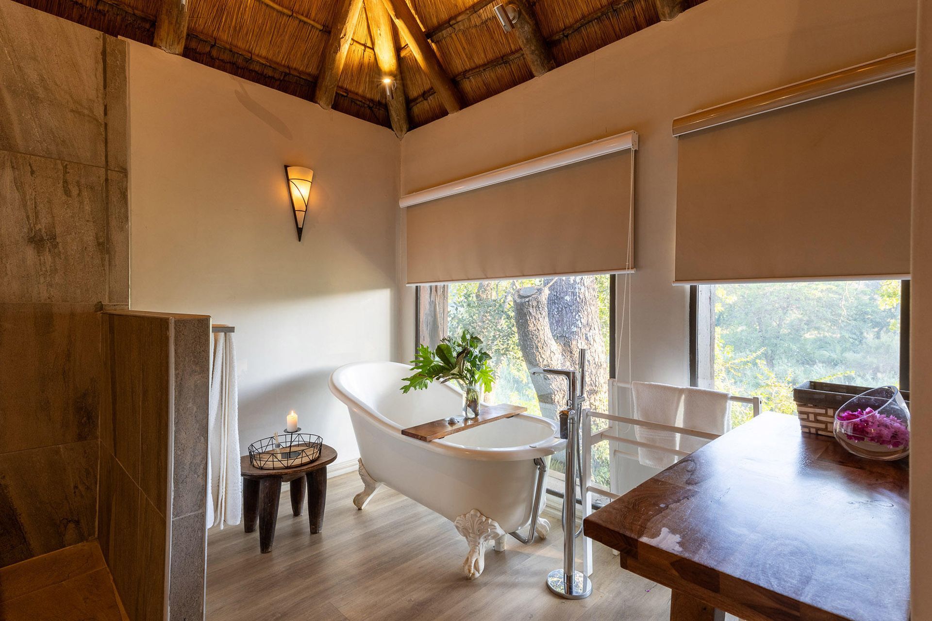 Tropical spa bathroom with a freestanding tub, warm wood ceiling, and large windows with blinds