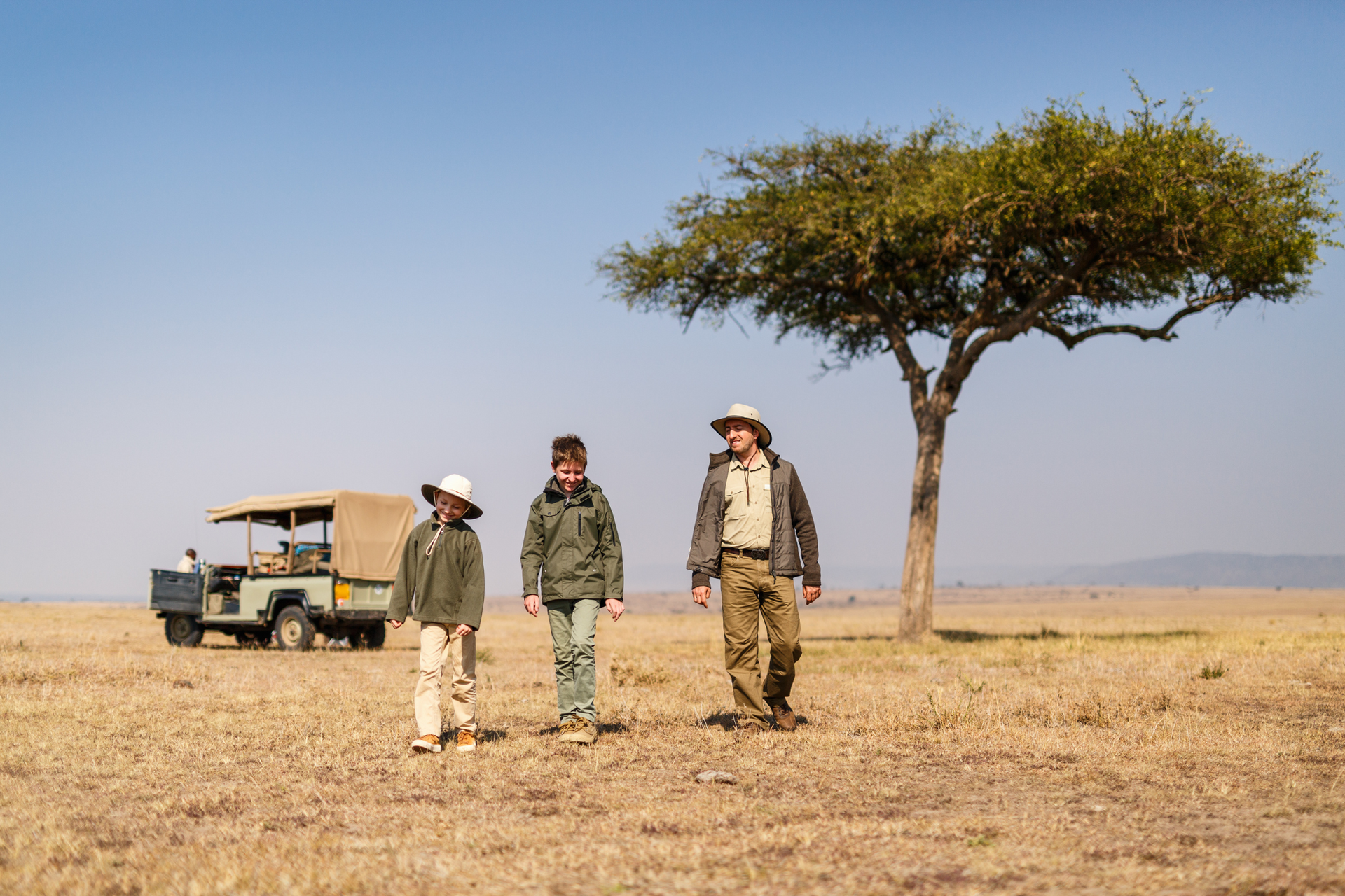 A group of people are walking in a field with a tree in the background. Family Friendly Safari
