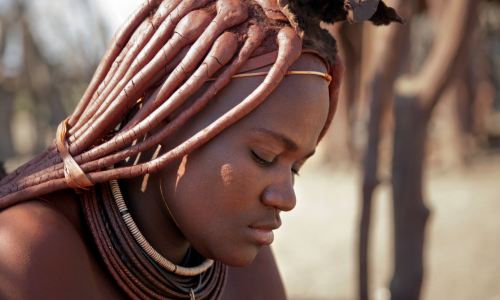 A woman with dreadlocks and a necklace is looking down.