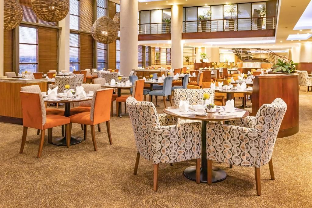 Restaurant interior with round tables, chairs, and decorations. Includes orange and patterned chairs, and a beige carpet.
