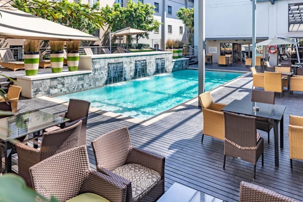 Outdoor patio with wicker chairs, tables, and swimming pool. Buildings, trees, and blue water.