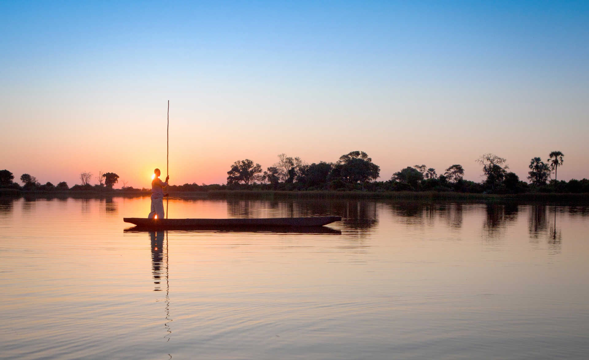 Sunset over a calm river with a small boat silhouetted against orange and blue sky