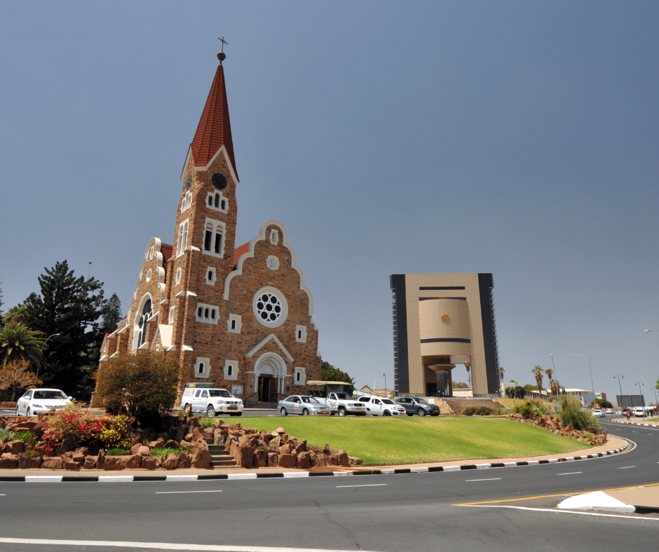 Red-brick church with tall steeple beside a modern building on a landscaped roundabout under a clear sky
