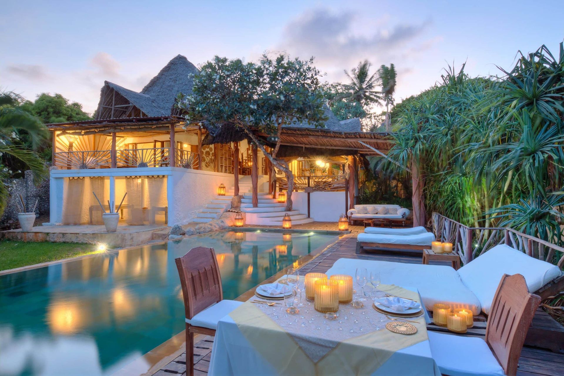 A table with candles on it in front of a large house with a swimming pool.