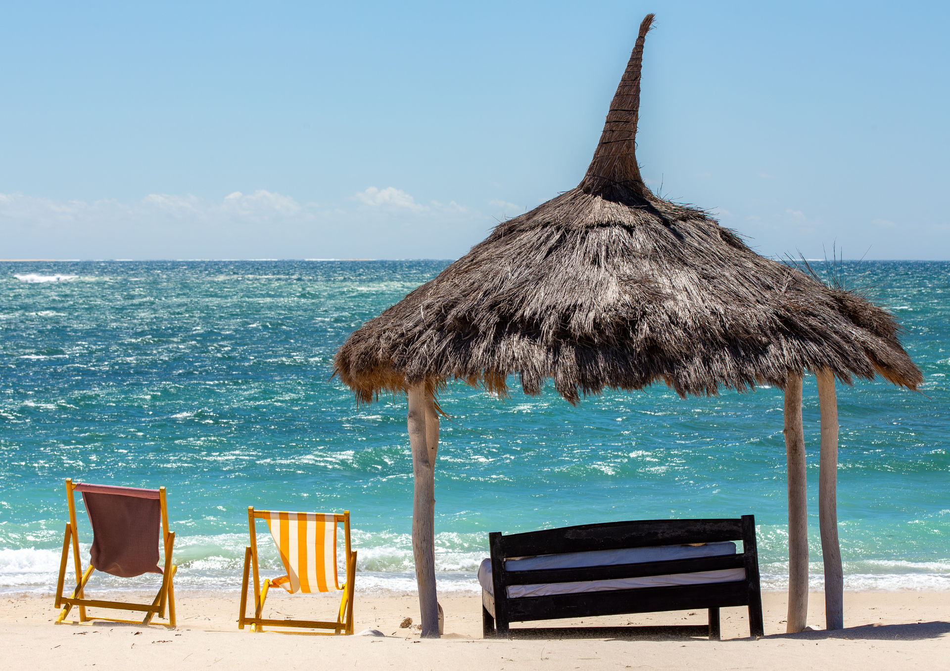 A beach with chairs and a bench under an umbrella