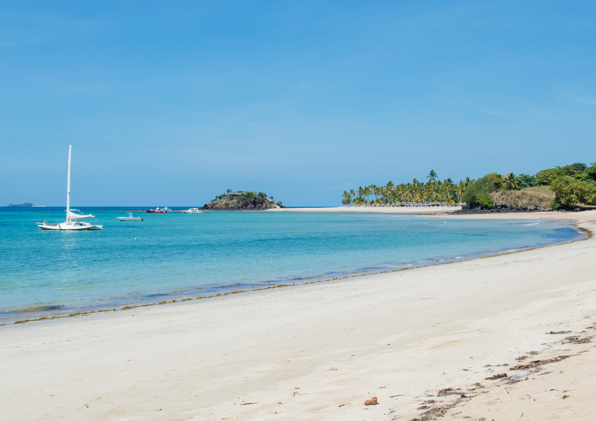 A sailboat is floating on the water near a beach.