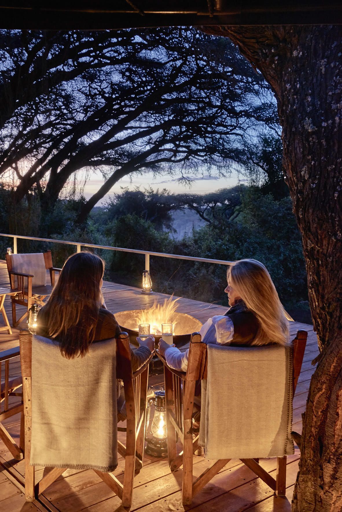 Two women are sitting at a table with a fire pit in the background. Ngorongoro Crater