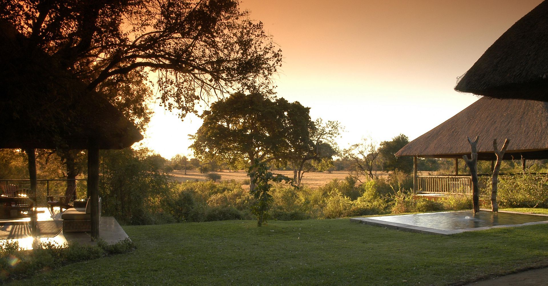 A sunset over a lush green field with thatched roofs