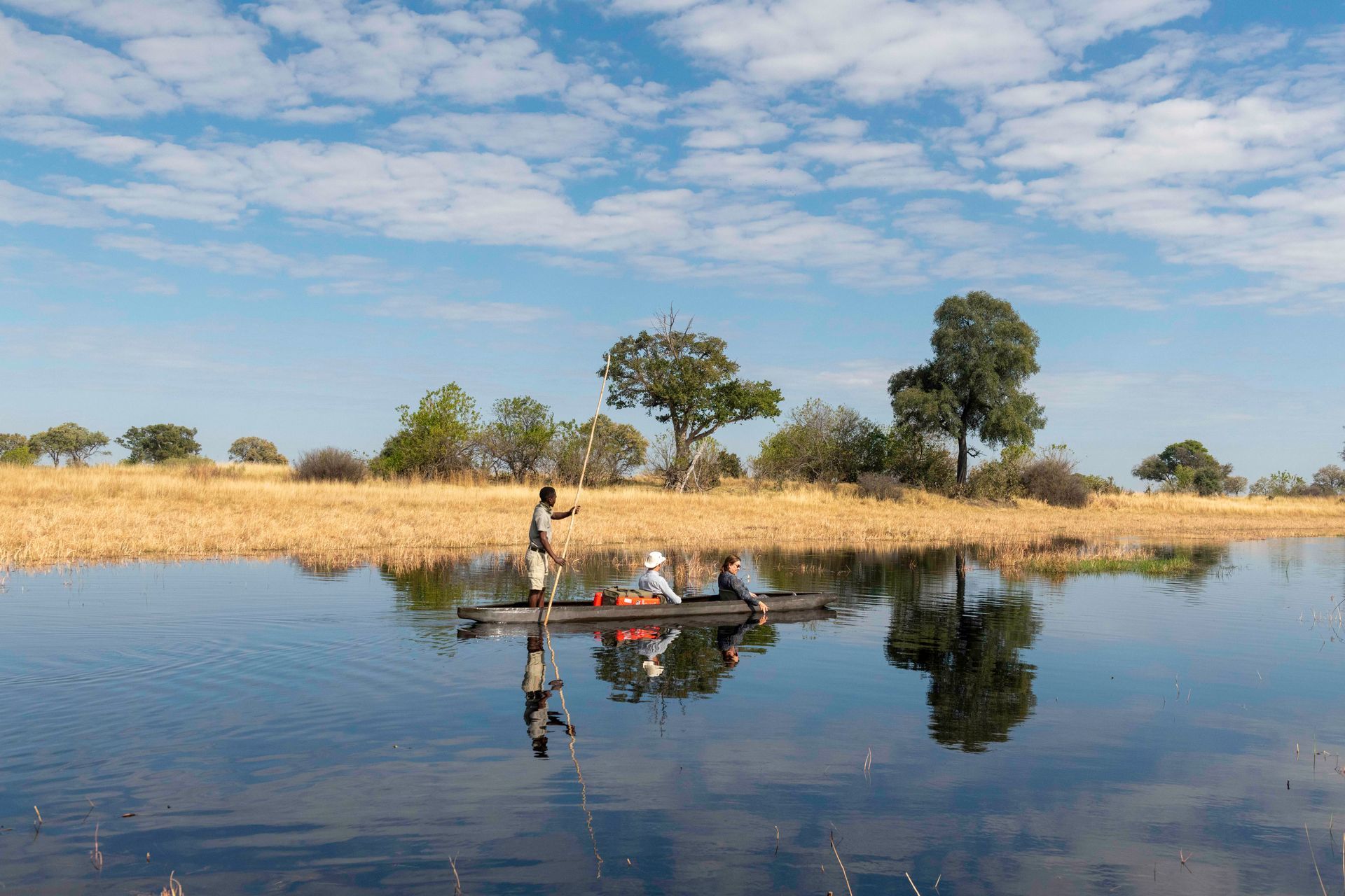 People in a canoe on a still river, with reflections of trees and sky.