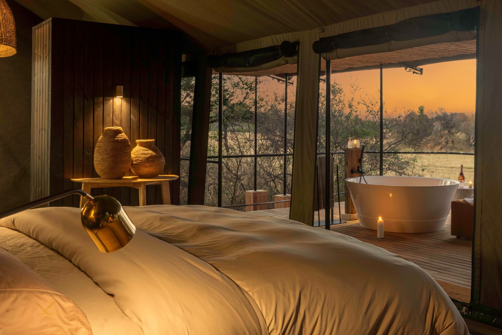 Bedroom with bed, open view of nature, and outdoor bathtub at sunset.