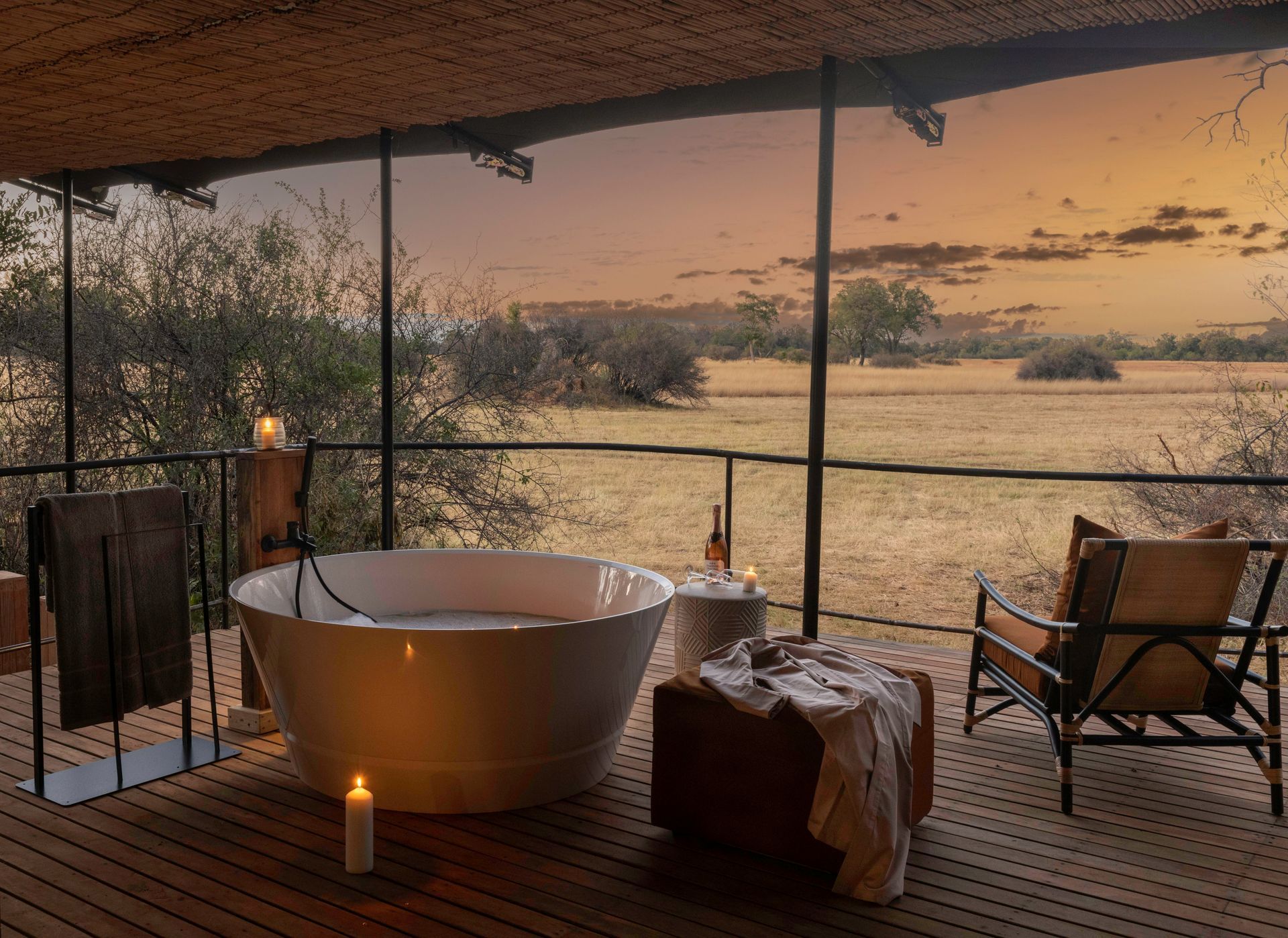Outdoor bathtub on a deck overlooking a savanna at sunset.