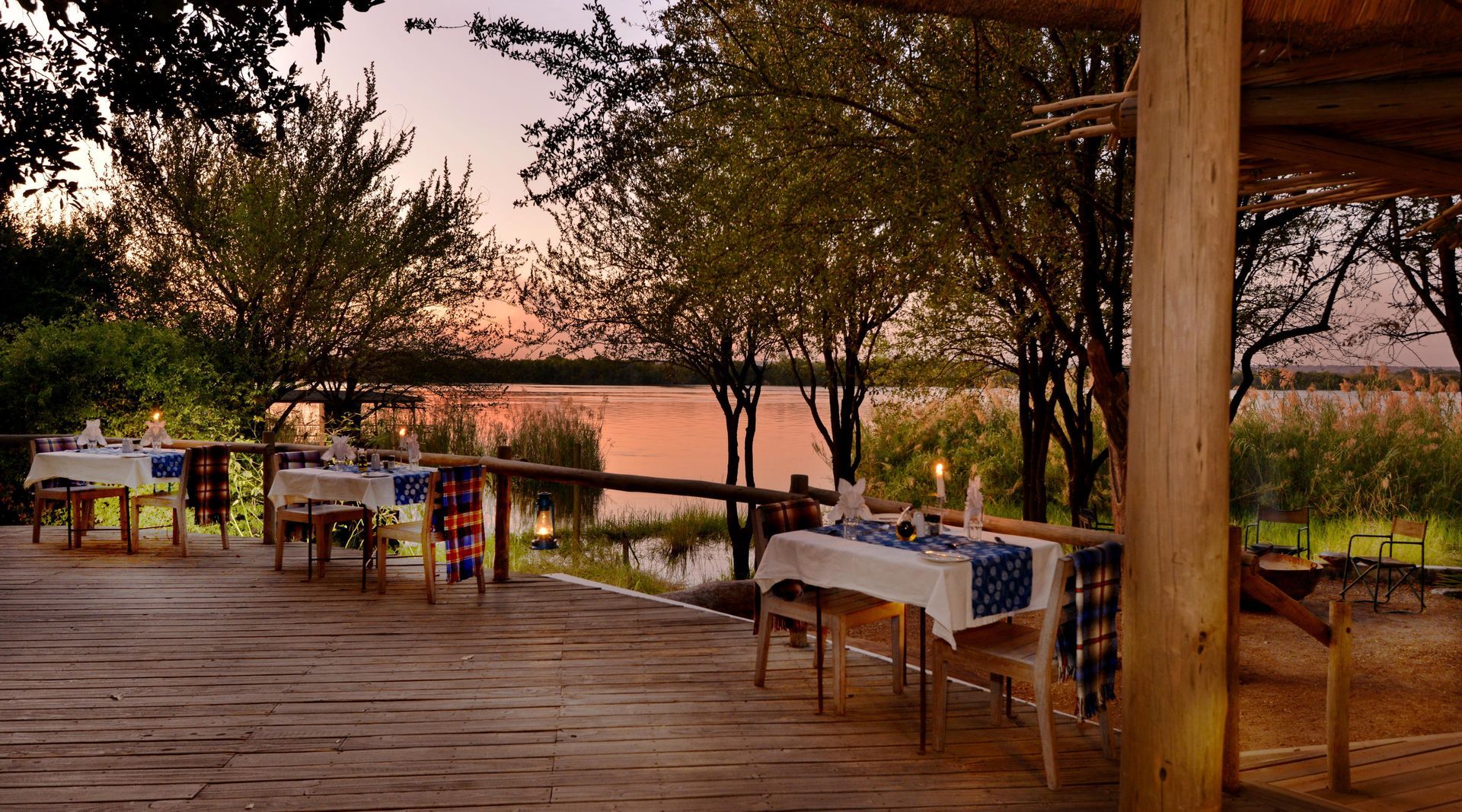 Outdoor dining setting by water at sunset. Tables set with white tablecloths and blue accents.