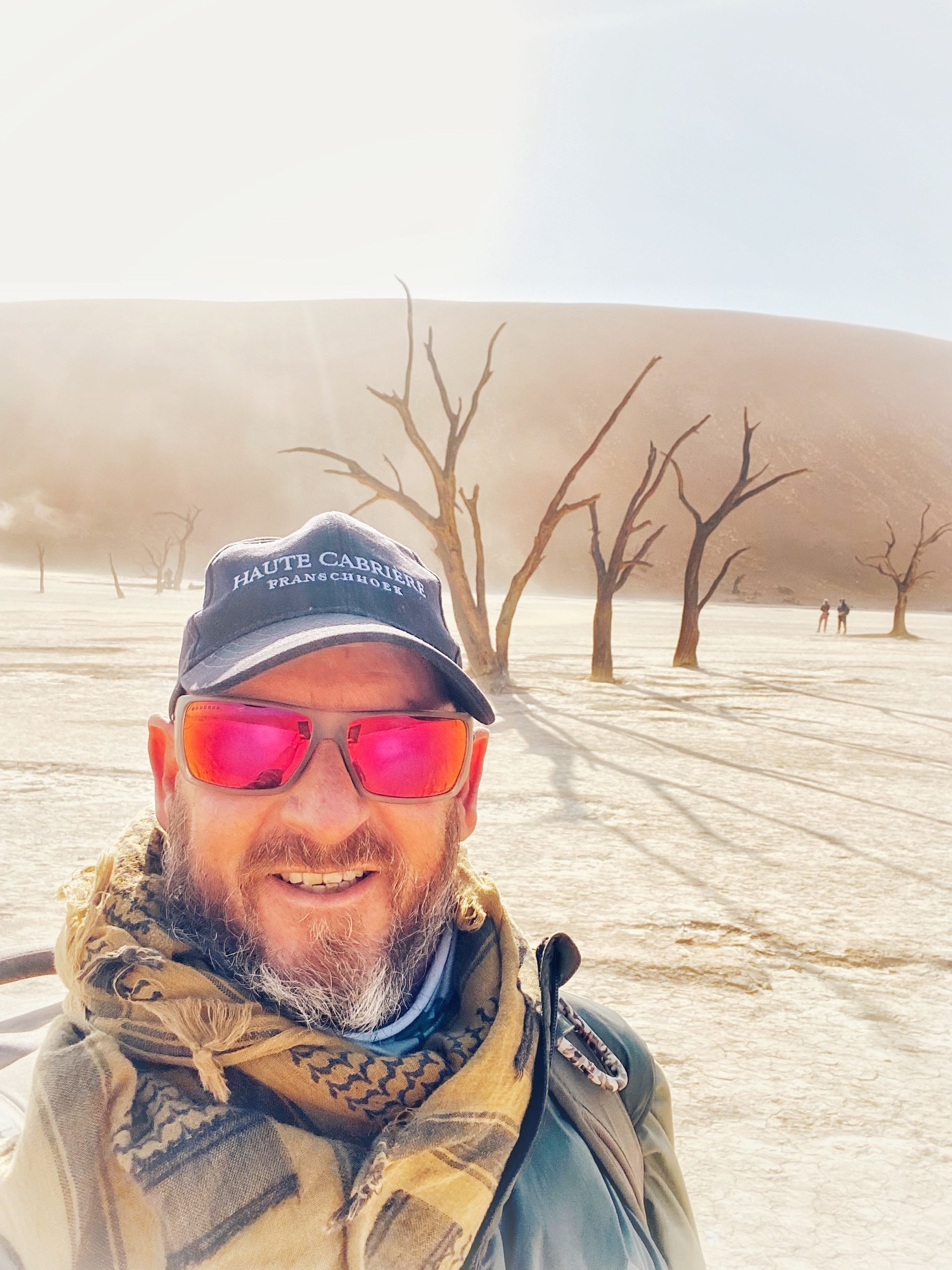 A man wearing sunglasses and a hat is standing in the desert. Namibia Safari