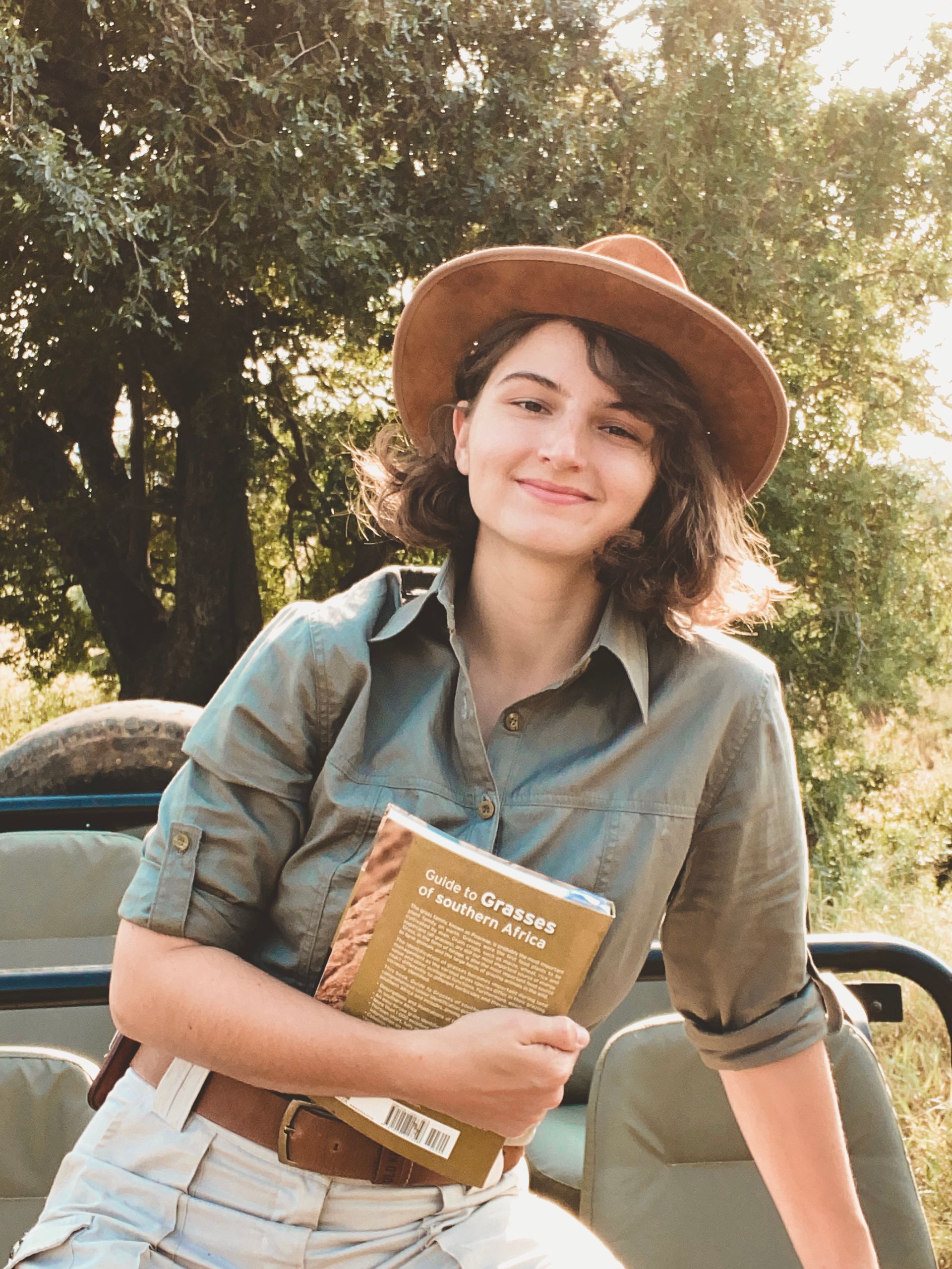 a woman in a hat is sitting on a jeep holding a book .
