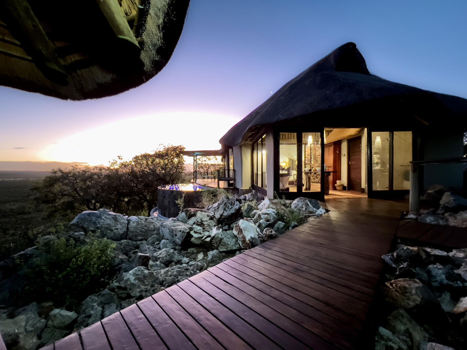 A house with a thatched roof and a wooden walkway leading to it Namibia Safari
