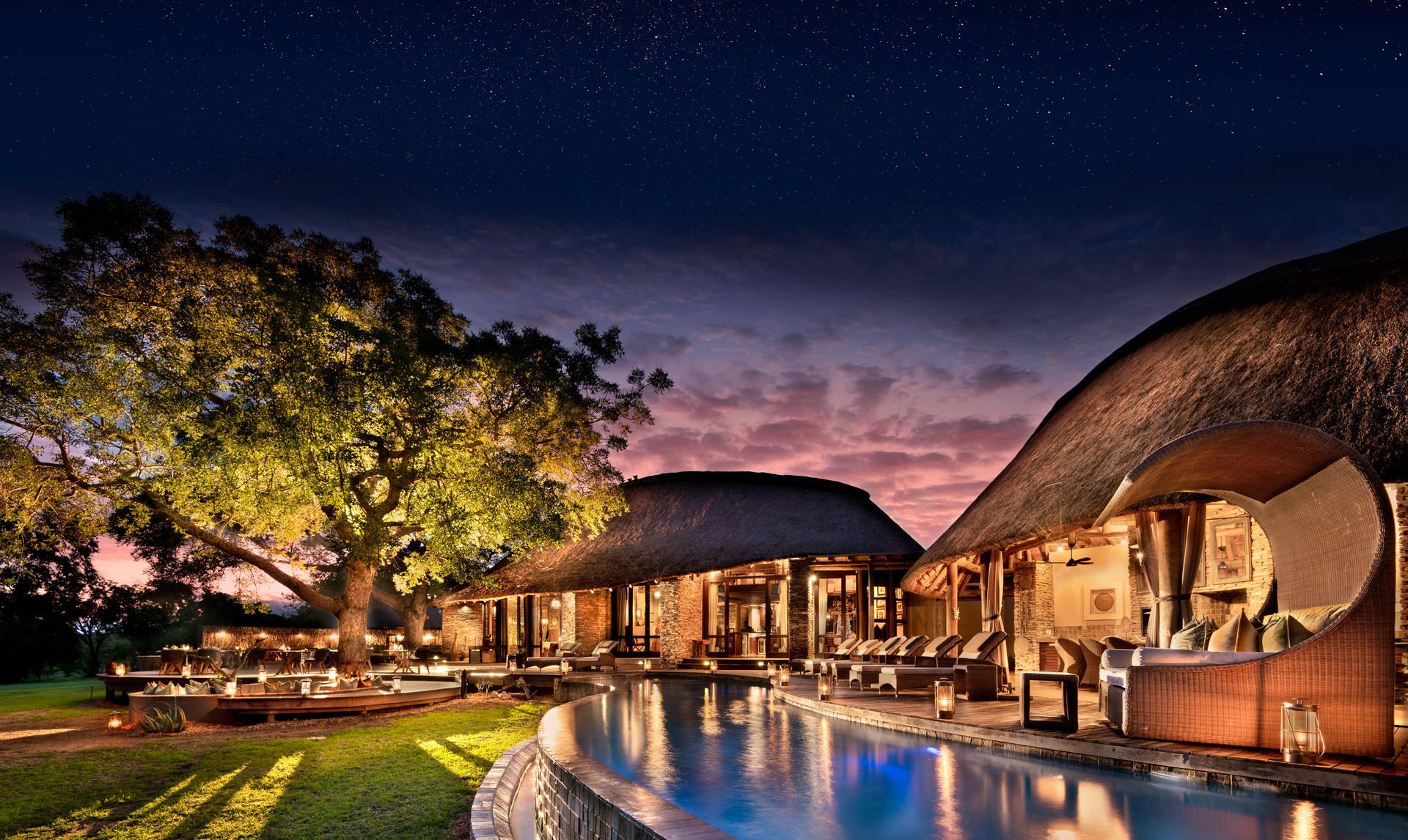 Luxury safari lodge at night with a pool, thatched roofs, and a starry sky.