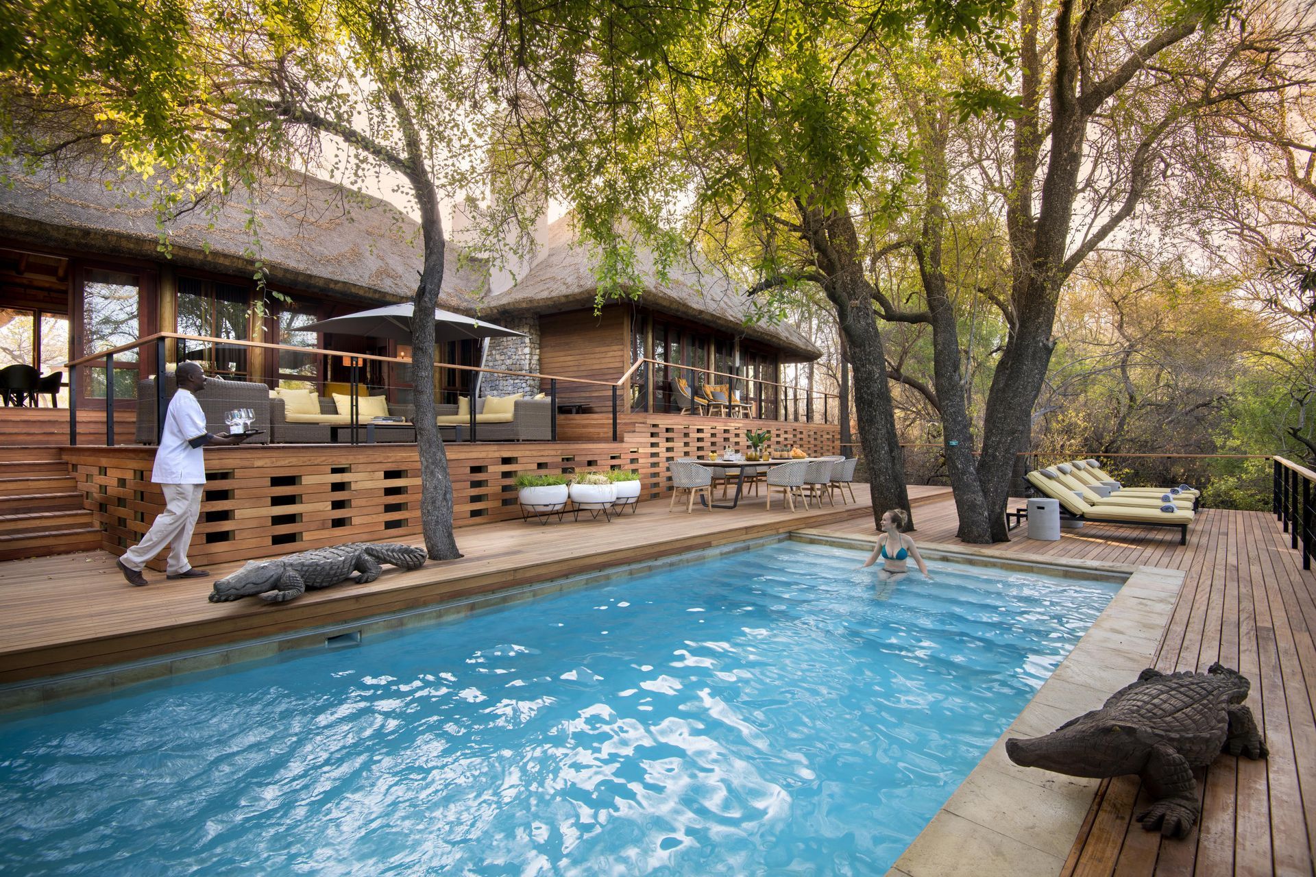 A large swimming pool is surrounded by trees and a wooden deck. Malaria Free Safari Destinations