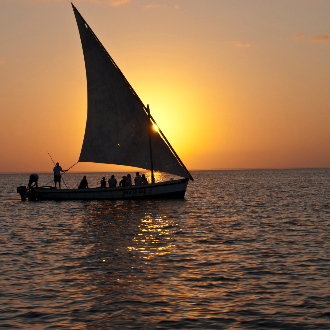 A sailboat is floating in the ocean at sunset