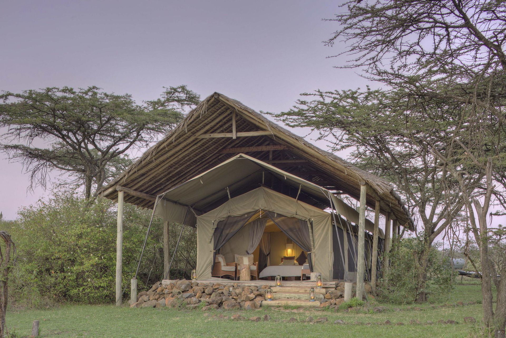 A tent is sitting in the middle of a field surrounded by trees. Luxury African Safaris