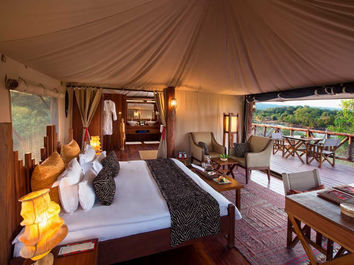 Luxurious tent interior overlooking a scenic view with a bed, seating area, and wooden furniture.