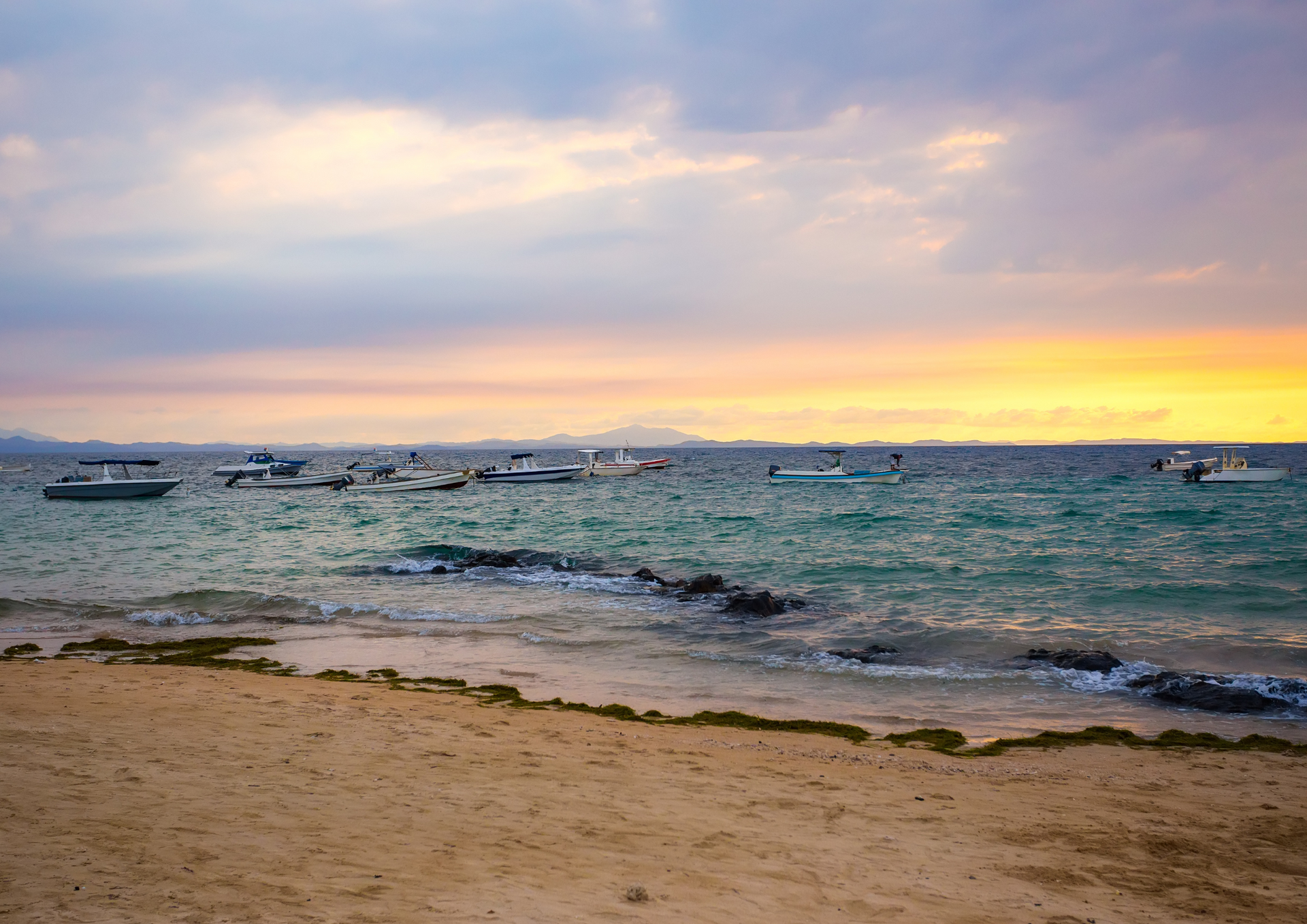 There are many boats in the ocean at sunset.