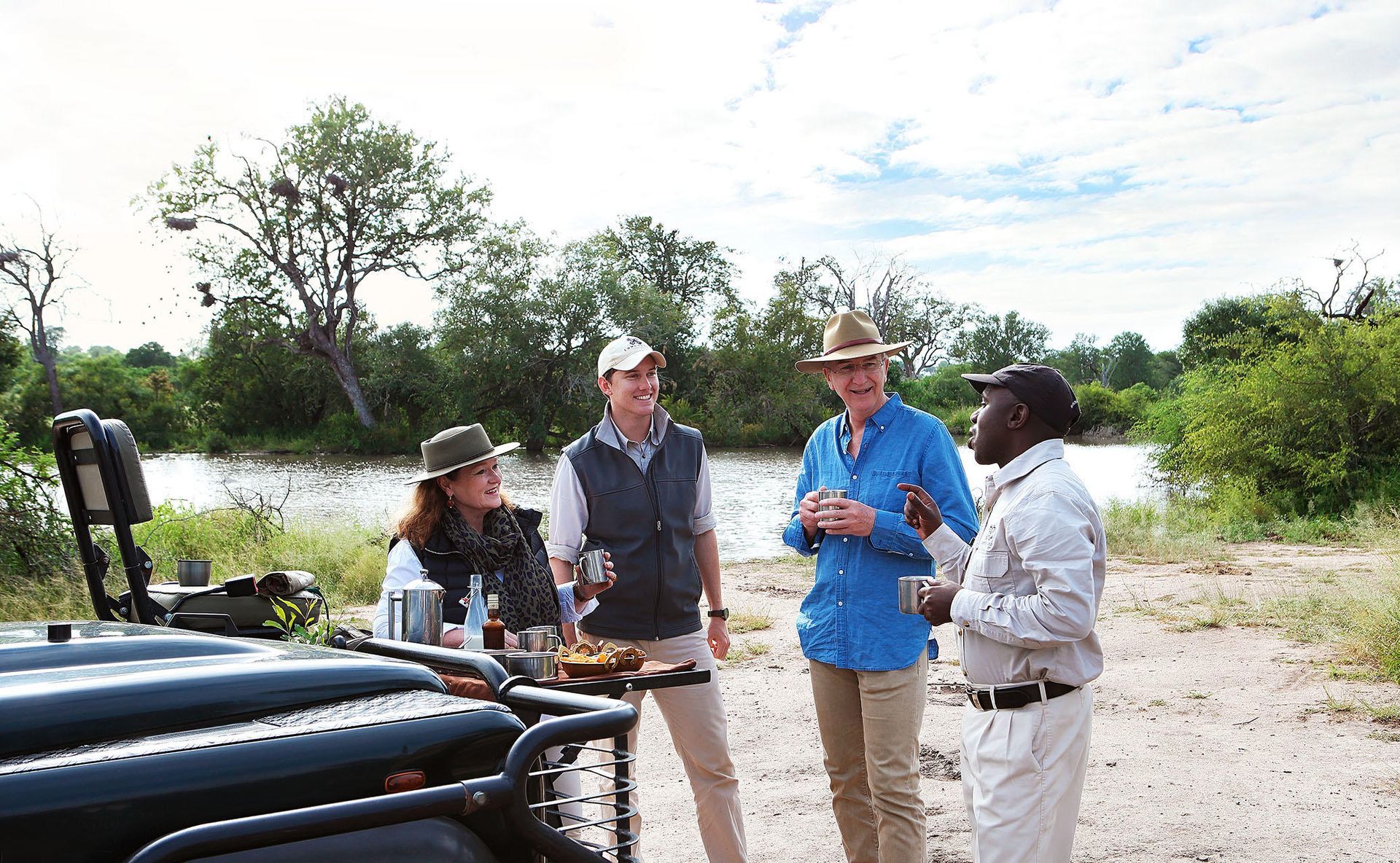 People enjoying drinks and snacks on safari near a river.