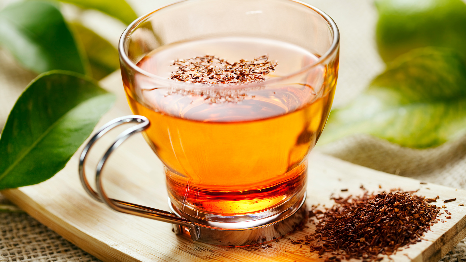 A cup of tea is sitting on a wooden cutting board next to a pile of tea leaves.