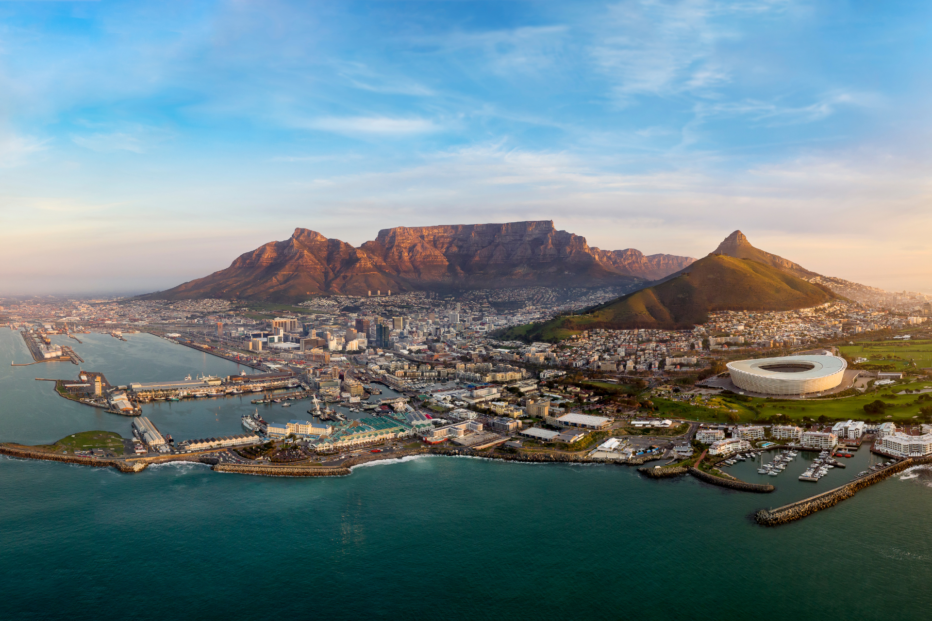 Aerial view of Cape Town’s waterfront with Table Mountain under a blue sky at sunset