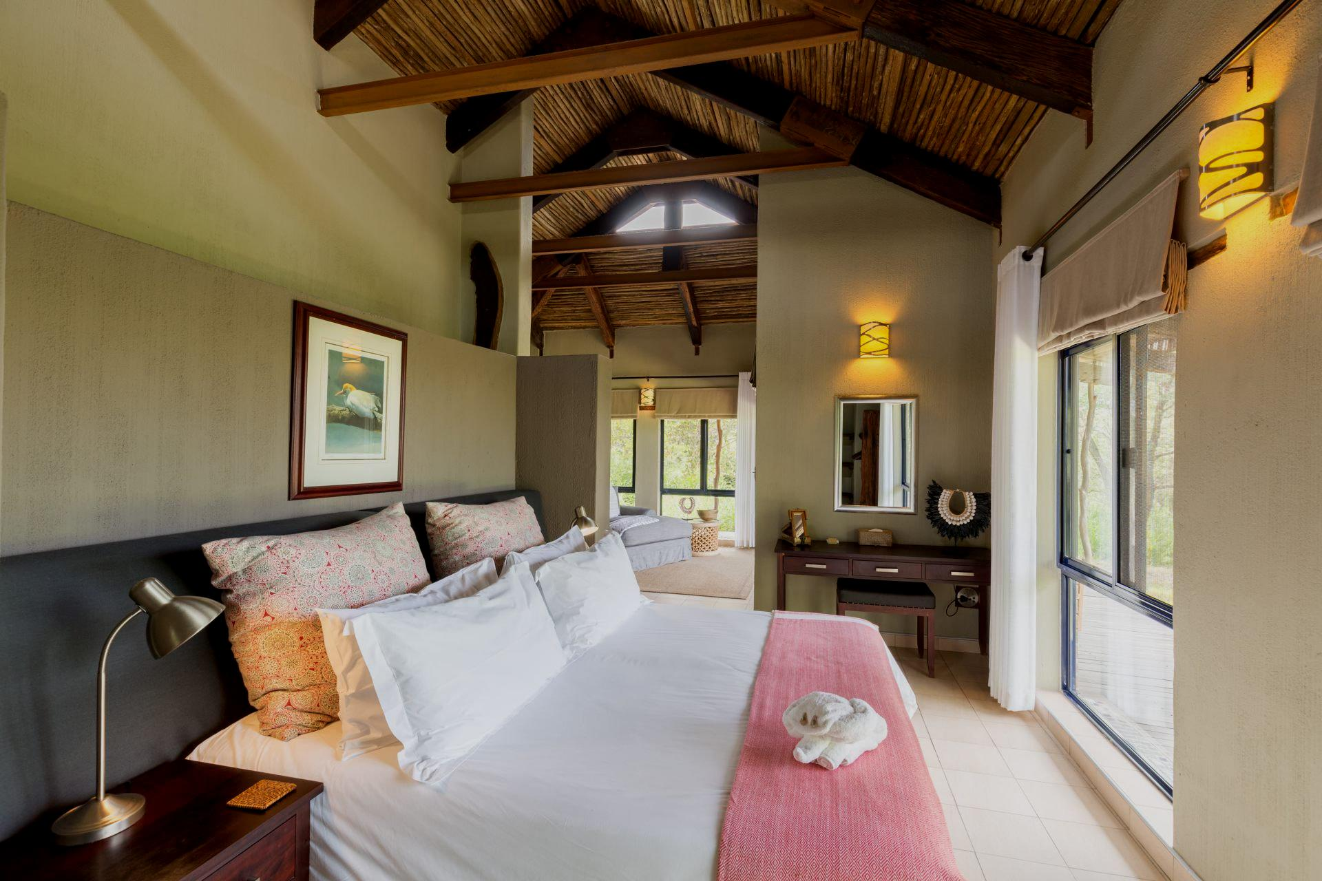 Bedroom with a large bed, natural light, and a view to a bathroom. Rustic decor with light colors and wood accents.