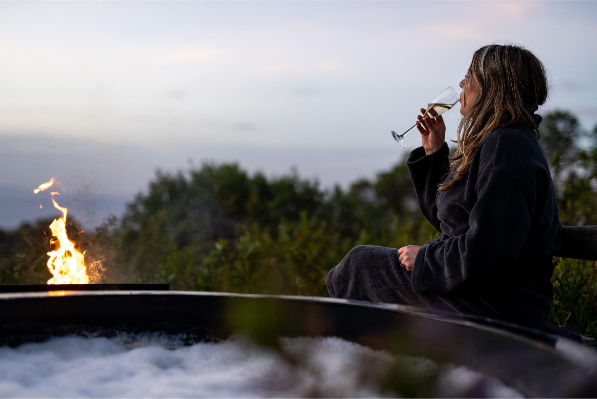 A woman is sitting in a hot tub drinking wine and looking at a fire Ngorongoro Crater